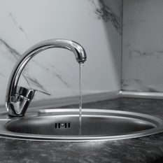 Chrome faucet with running water in a modern kitchen with marble countertop.