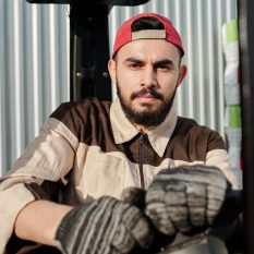Focused male worker in uniform operates forklift in industrial setting.