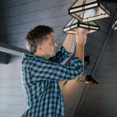 Adult man changing bulb in pendant light fixture, modern home interior setup.